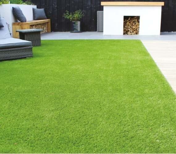 Modern outdoor patio area featuring 30mm (Maldives) artificial grass with lounge seating and a fireplace.